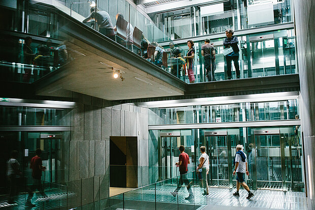 
            
                Blick ins mumok Treppenhaus auf die gläsernen Aufzüge, auf zwei Ebenen sind Menschen zu sehen, die im Museum herumgehen
            
        