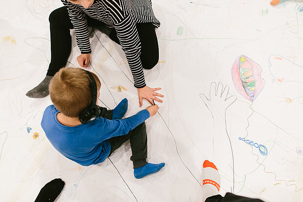 
            
                Kinder sitzen auf dem Boden mit einer Papierunterlage und zeichnen
            
        