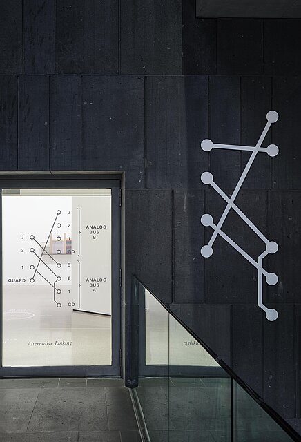 Entrance to the exhibition space with a glass door, the grey basalt stones of the mumok building can be seen on the right 