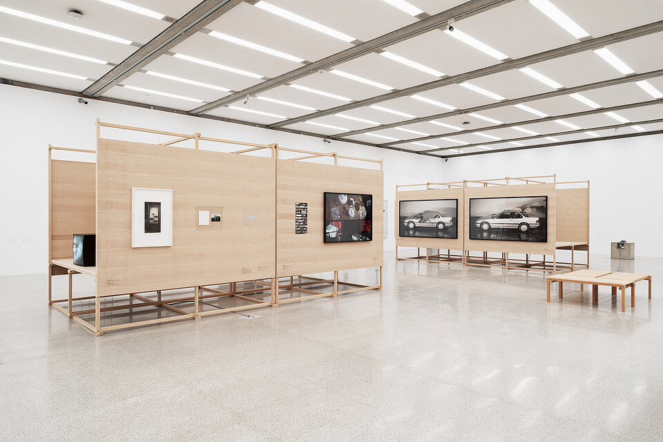 Bright exhibition space with displays made of light-coloured wood, with various works of art on top that are difficult to recognise