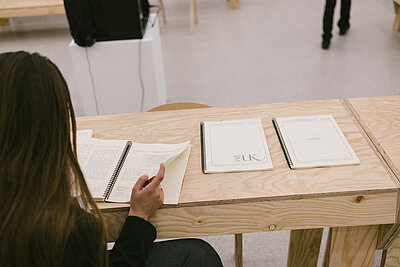 Eine Frau sitzt im Ausstellungsraum an einem Holztisch und blättert in einer Broschüre