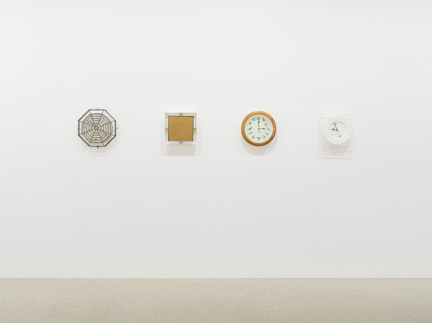 Four differently designed clocks hang on a white wall. 