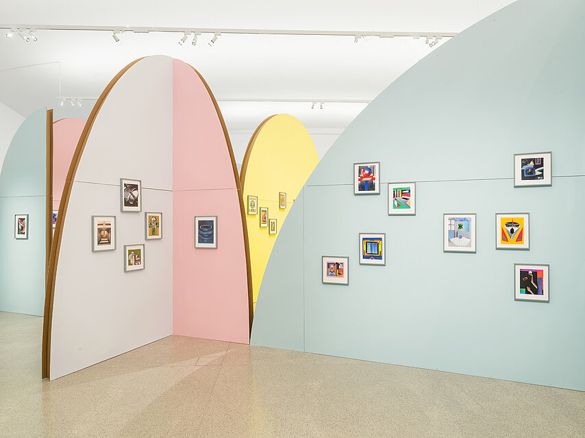 Semicircular cardboard walls in pastel colours in the exhibition space, colourful collages in A4 format on the walls