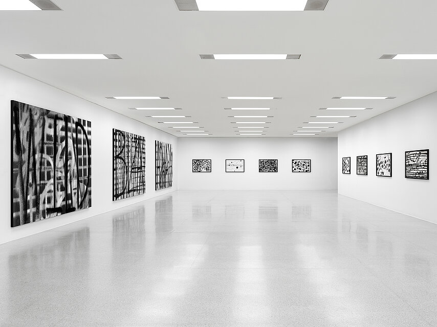 View into an exhibition room with white walls and a light-coloured floor, black and white abstract works of art hang on the walls