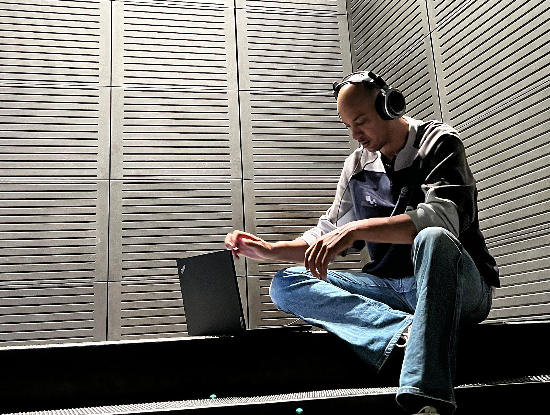 junger Mann sitzt auf Treppe, trägt Kopfhörer und arbeitet am Laptop