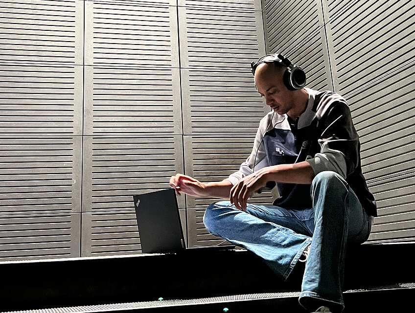 junger Mann sitzt auf Treppe, trägt Kopfhörer und arbeitet am Laptop