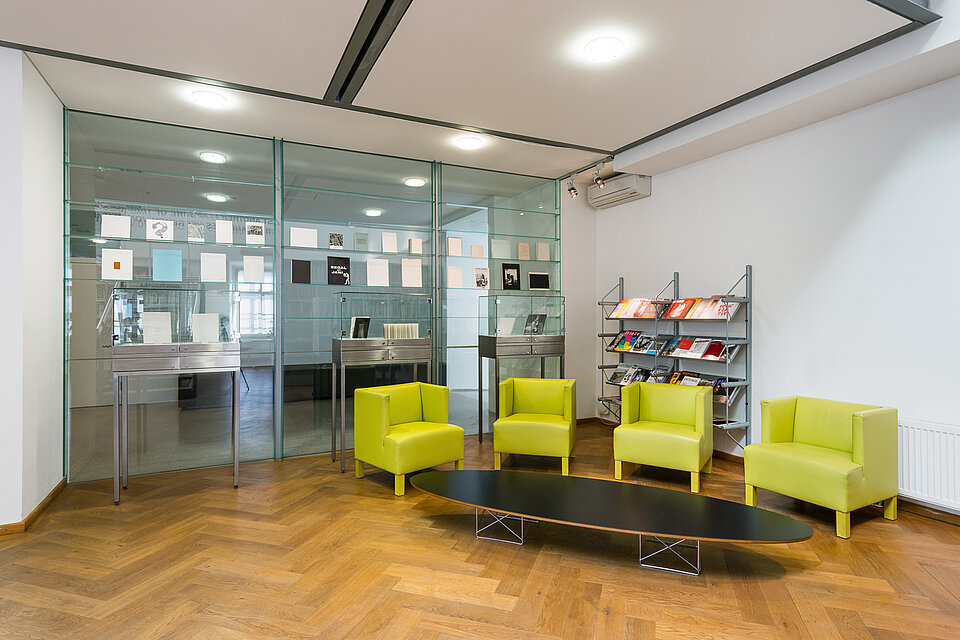 Sitzecke in der mumok Bibliothek, hellgrüne Sessel um einen niedrigen Tisch gruppiert, im Hintergrund eine Glaswand, davor Bücherdisplays