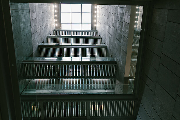 
            
                Blick von unten ins Treppenhaus des mumok, hoher Schacht mit dunklen Wänden und Treppen
            
        