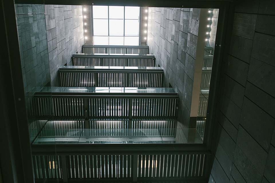 Blick von unten ins Treppenhaus des mumok, hoher Schacht mit dunklen Wänden und Treppen