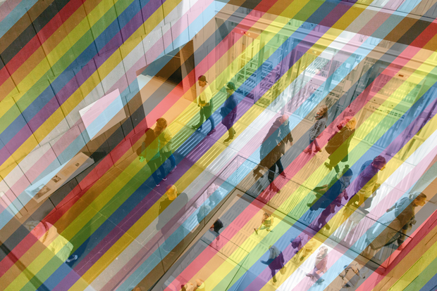 
            
                Blick ins Treppenhaus des mumok mit verglasten Fahrstühlen, es gehen mehrere Menschen auf unterschiedlichen Ebenen herum. Das Bild ist mit einem transparenten Regenbogen versehen.
            
        