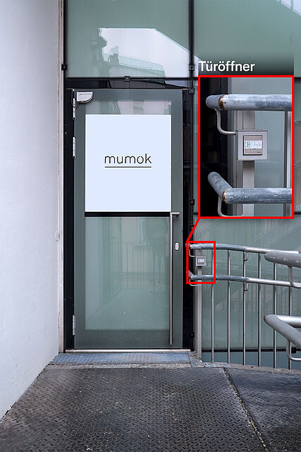 Gläserne Eingangstür mit „mumok“-Beschriftung neben einem Geländer, hervorgehoben ist ein Türöffner‑Taster an der Metallkonstruktion. / Glass entrance door labeled “mumok” next to a railing, with a door opener button on the metal structure highlighted.