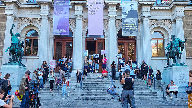 
            
                Menschen am Haupteingang eines alten Gebäudes während einer Performance
            
        