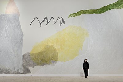 Die Künstlerin steht vor einem großen Wandbild von ihr mit dem Namen Sun and Moon. Schematisch sind im Zacken im Bild zu sehen.