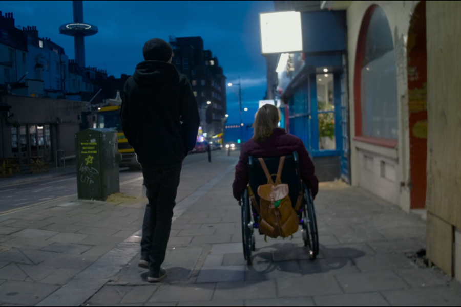 a person standing on the left, a person using a wheelchair on the right