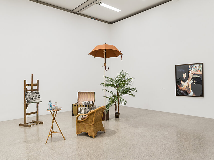 various everyday objects in the exhibition room, several armchairs, a plant and a parasol