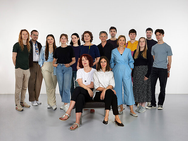 
            
                eine Gruppe von Personen vor einer weißen Wand, vier davon sitzen im Vordergrund auf einer Bank: Das Team Marketing und Kommunikation im mumok
            
        