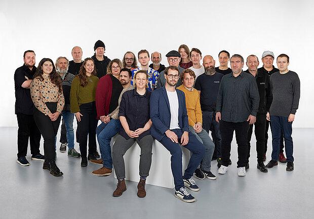 
            
                eine Gruppe von Personen vor einer weißen Wand, vier davon sitzen im Vordergrund auf einem Sockel: das Team Technik und Betrieb im mumok
            
        