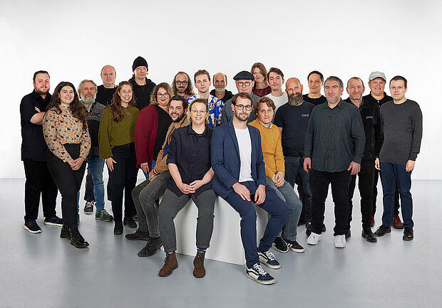 
            
                a group of people in front of a white wall, four of them sitting on a pedestal in the foreground: the mumok's technology and operations team
            
        