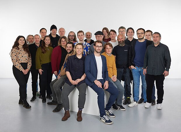 
            
                a group of people in front of a white wall, four of them sitting on a pedestal in the foreground: the mumok's technology and operations team
            
        