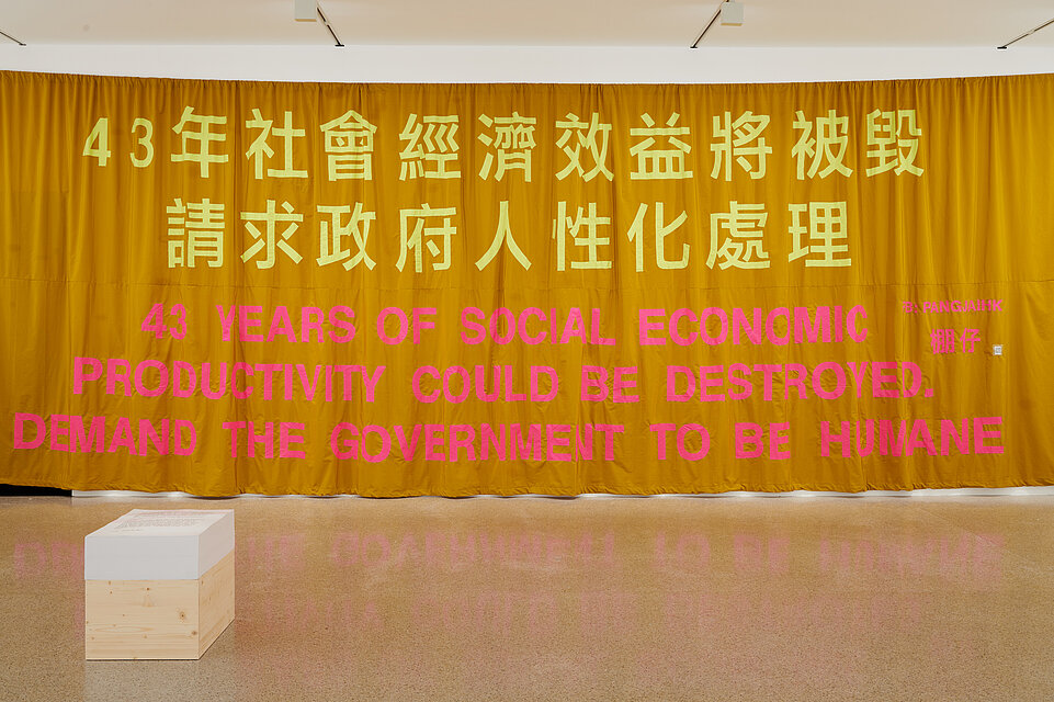 ein großer Gelber Vorhang mit chinesischen Schriftzeichen und der englischen Aufschrift in rot: 43 years of social economic productivity could be destroyed. demand the government to be humane