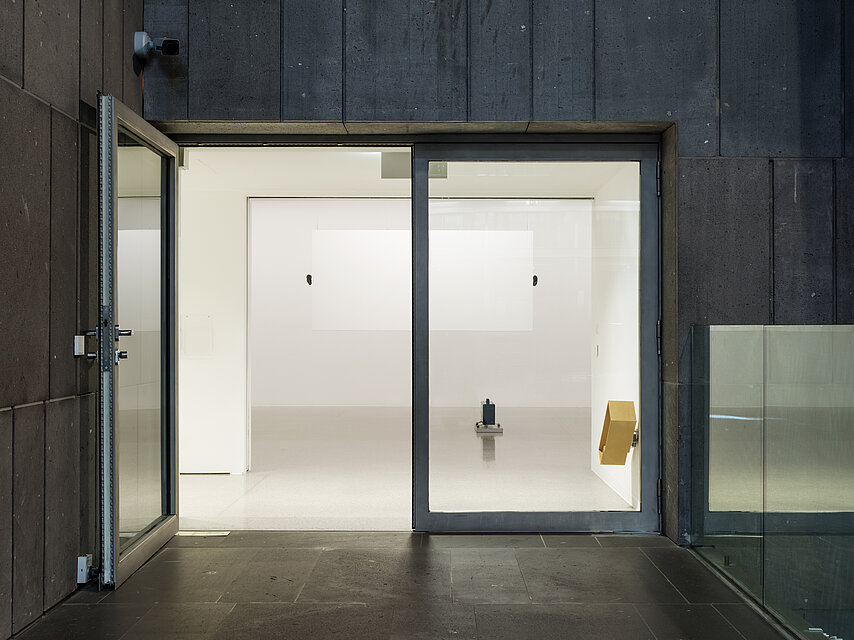 A large open glass door. Behind it, the white exhibition room and two works of art.