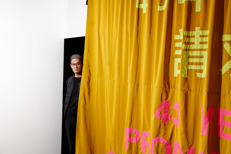  a large yellow curtain, a man peers out from behind it