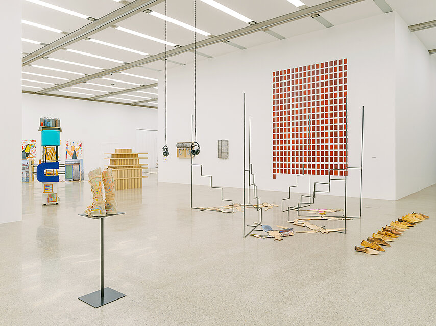  a bright exhibition space with various sculptures, with a large red work on the wall in the background