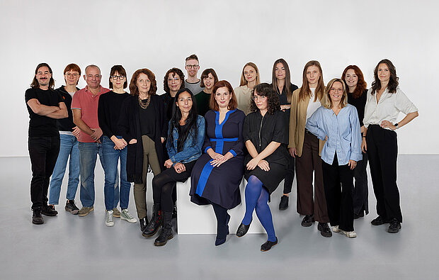 
            
                eine Gruppe von Personen vor einer weißen Wand, drei davon sitzen im Vordergrund auf einem Sockel, das Team Sammlung im mumok
            
        