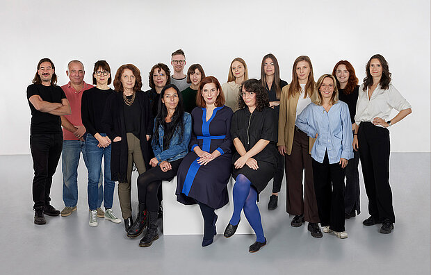 
            
                eine Gruppe von Personen vor einer weißen Wand, drei davon sitzen im Vordergrund auf einem Sockel, das Team Sammlung im mumok
            
        