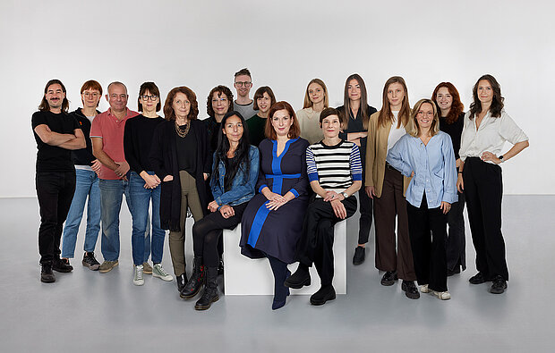 
            
                a group of people in front of a white wall, three of them sitting on a pedestal in the foreground, the team collection at mumok
            
        
