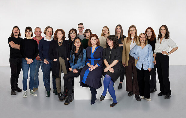 
            
                a group of people in front of a white wall, three of them sitting on a pedestal in the foreground, the team collection at mumok
            
        
