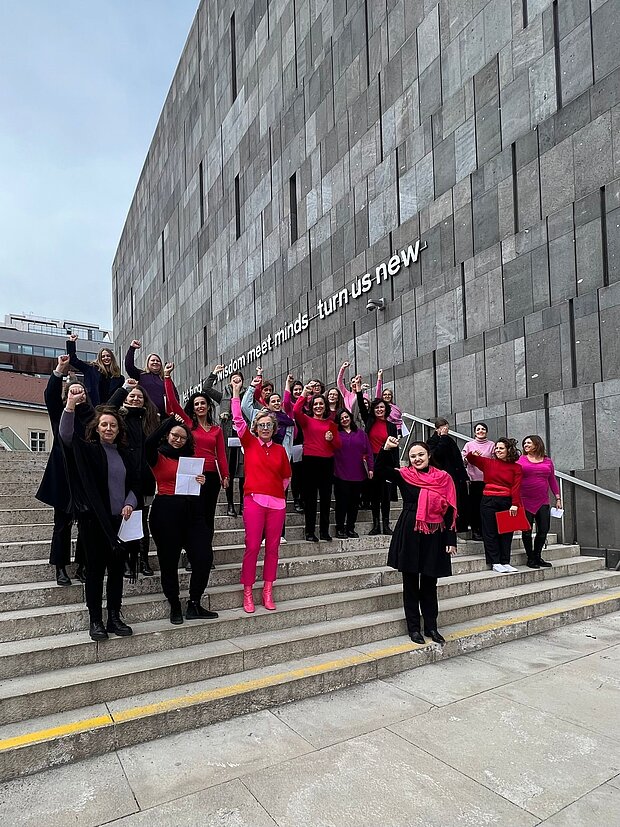 
            
                mehrere Frauen in pinker, roter und schwarzer Kleidung stehen auf der Treppe des mumok, manche haben ihre Faus geballt und strecken den Arm nach oben
            
        