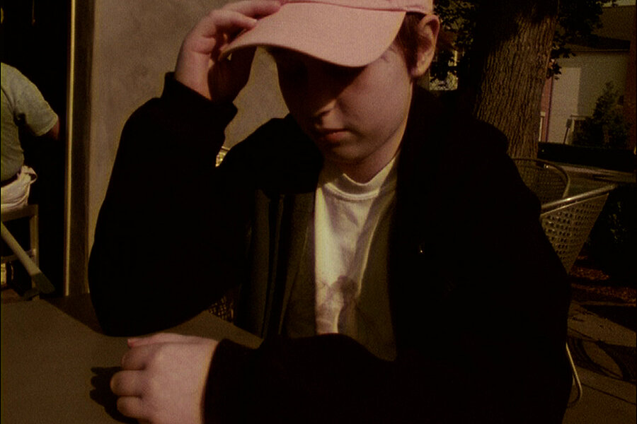 Person mit Baseballkappe sitzt an einem Tisch im Freien im warmen Abendlicht. / Person wearing a baseball cap sitting at an outdoor table in warm evening light.