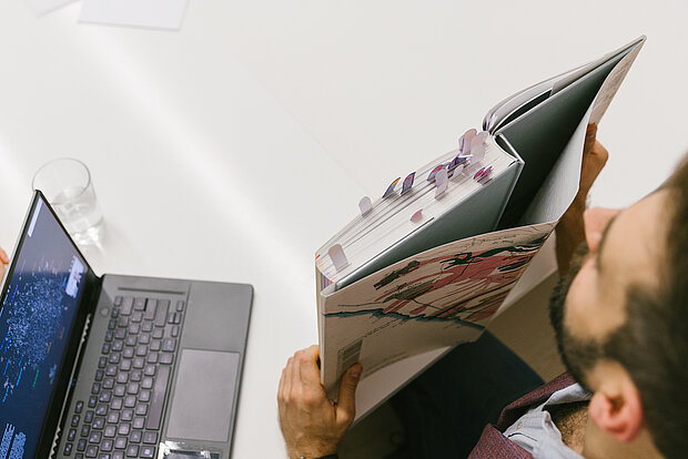 
            
                Ein junger Mann studiert Visualisierungen, links vorne ist ein Notebook zu sehen
            
        