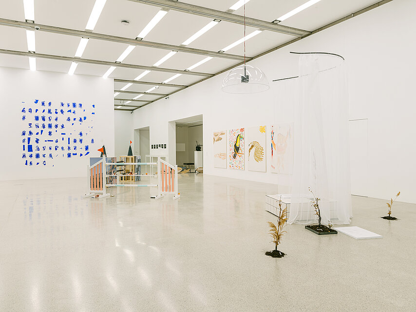 Exhibition view of a bright room, in the background an abstract painting in blue, in the foreground small sculptures