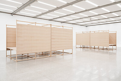 In einem weißen Ausstellungsraum sind vier große Objekte aus Holz platziert.