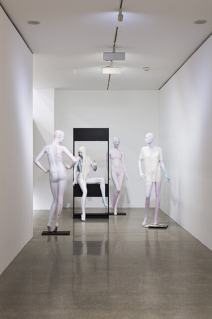  Four colourful mannequins are placed in front of a black frame. 
