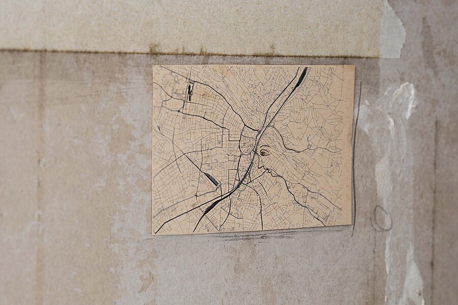 Kleine rechteckige Zeichnung auf gealtertem Papier, die ein dichtes Netz aus kartografischen Linien zeigt, in das das Profil eines menschlichen Gesichts eingezeichnet ist. / Small rectangular drawing on aged paper showing a dense network of cartographic lines with the profile of a human face integrated into the map structure.