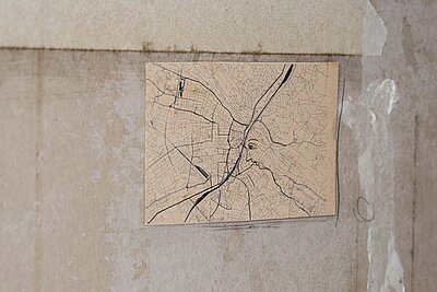 Kleine rechteckige Zeichnung auf gealtertem Papier, die ein dichtes Netz aus kartografischen Linien zeigt, in das das Profil eines menschlichen Gesichts eingezeichnet ist. / Small rectangular drawing on aged paper showing a dense network of cartographic lines with the profile of a human face integrated into the map structure.