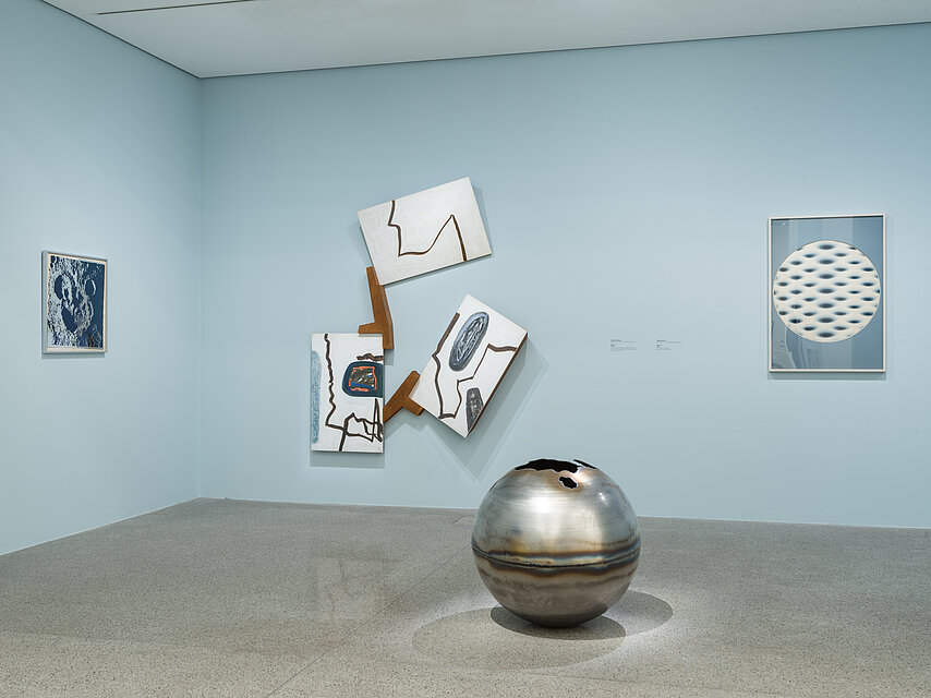 Light blue wall, a large silver sphere on the floor, abstract artwork on the wall in the background
