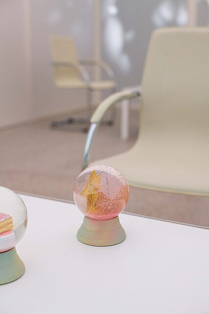 Two snow globes stand on a white table. Two beige armchairs can be seen in the background.