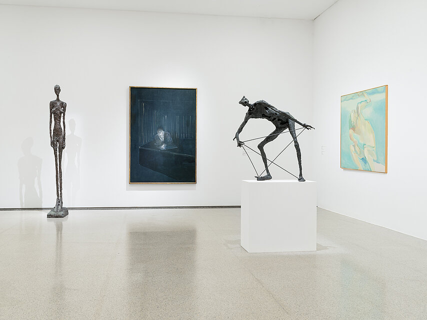Bright exhibition space, on the front right on a white base a black sculpture that appears human and bends over, on the right on the wall a light green painting, in the centre on the wall a dark blue painting, on the left on the wall a human-sized, filigree, black sculpture of a standing person