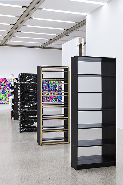 Four empty black bookshelves. Behind them are large, colourful pictures on the walls.