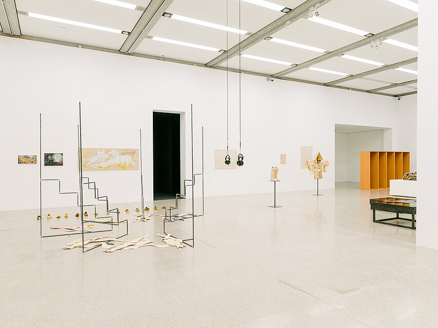 Bright exhibition space with various sculptures, a passageway in the centre leads into a black room