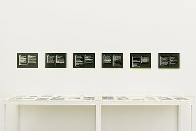 Six black and white pictures hang on a white wall above a white display case