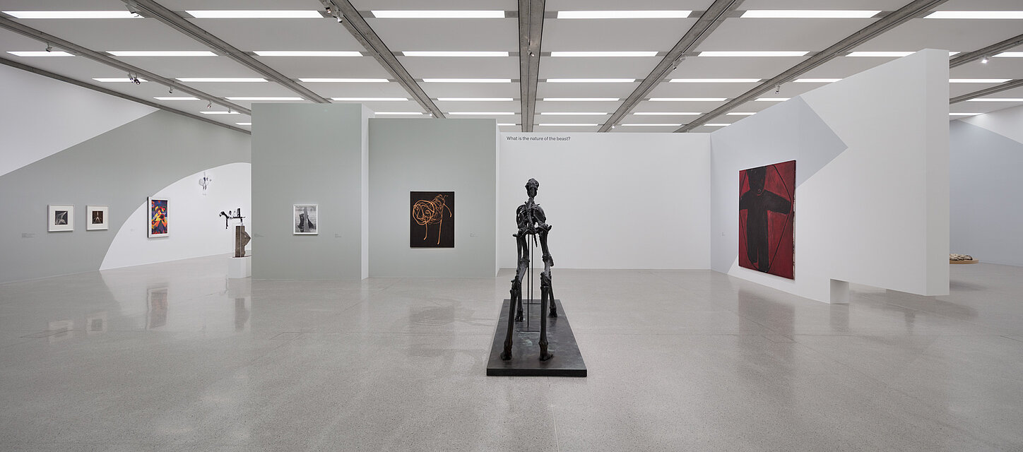 White exhibition room with paintings in various formats on the walls. An abstract sculpture is placed in the centre of the room. 