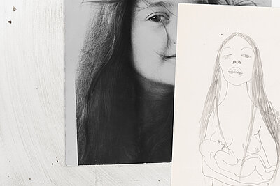 Teilansicht eines schwarz-weißen Porträts auf Papier, links ein Auge und Haarpartien, rechts überlagert von einer einfachen Bleistiftzeichnung einer stehenden menschlichen Figur. / Partial view of a black-and-white portrait on paper, showing an eye and hair on the left, overlaid on the right by a simple pencil drawing of a standing human figure.
