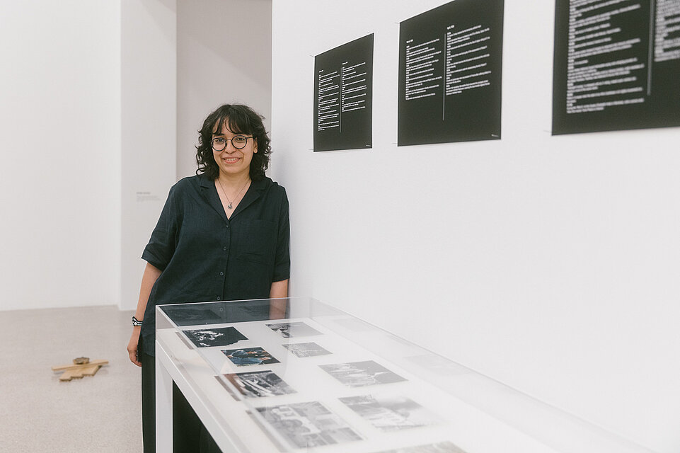 Artist Huda Takriti stands behind a display case containing her works