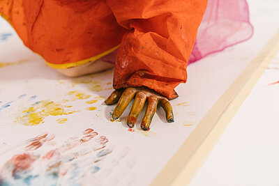 Eine Kinderhand mit Farbresten, das Kind scheint auf weißem Untergrund zu malen