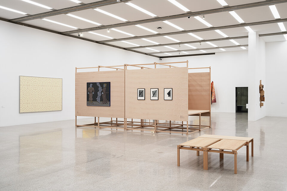  a bright exhibition space with light-coloured wooden displays, with various works of art in black and white on top